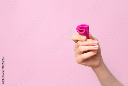 Mature content A young woman folding a pink menstrual cup in her hand. Pink colored background. Space for text. Eco-friendly silicone women's health cycle photo
