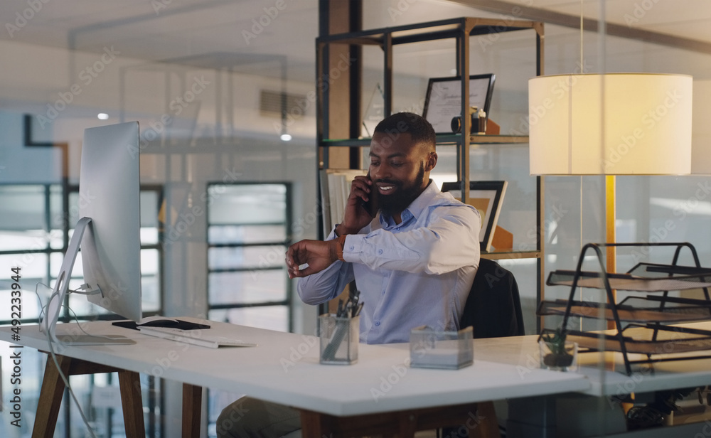 I wont be here too long. Shot of a young businessman checking the time on his wristwatch while talking on a cellphone in an office at night. I wont be here too long. Shot of a young businessman checking the time on his wristwatch while talking on a cellphone in an office at night.