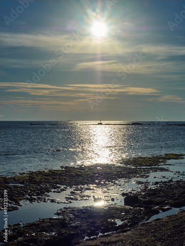 A setting sun with beams reflected into a golden pathway reaching from the horizon to a rock outcrop in a rippled sea.