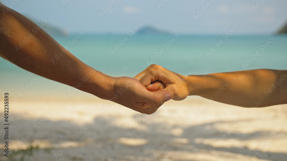 Hands of flirting young man and woman touching on beach in palms shadow against calm azure ocean close view. Traveling to tropical countries Hands of flirting young man and woman touching on beach in palms shadow against calm azure ocean close view. Traveling to tropical countries