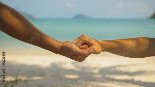 Hands of flirting young man and woman touching on beach in palms shadow against calm azure ocean close view. Traveling to tropical countries © ivandanru