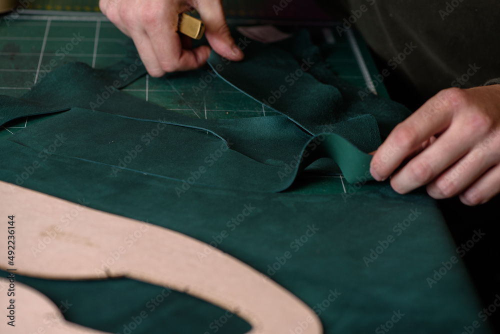 Shoemaker cutting suede leather with craft knife for handmade shoes in workshop. Making bespoke shoes. Closeup.