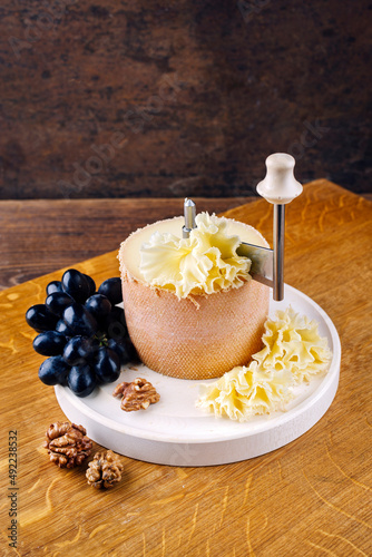 Traditional tete de moine aged mountain cheese of the Alps served with grapes on a girolle on a wooden board