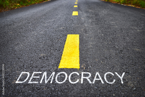 Democracy word on asphalt road with yellow line marking on road surface