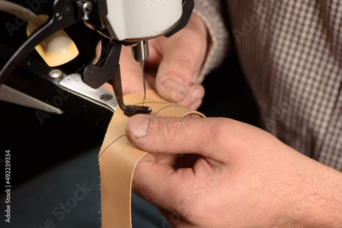 Obraz na płótnie Industrial sewing machine in workshop of shoemaker. Bootmaker setting up professional sewing equipment on factory. Closeup of hands stitching leather. Selective focus. w salonie