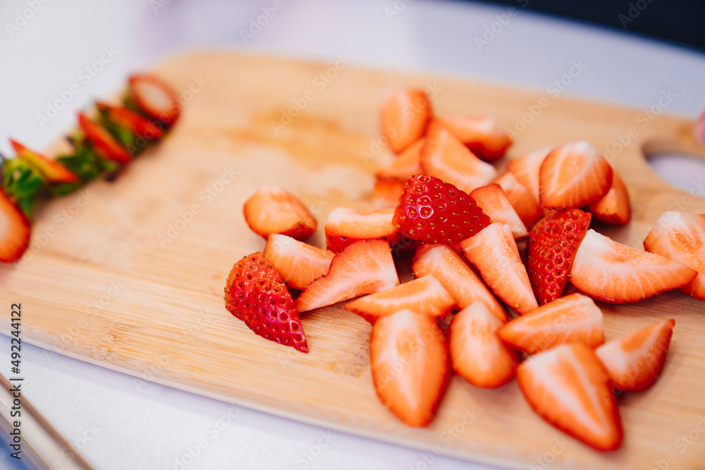 strawberries are cut into pieces on a wooden cutting board to decorate desserts.
