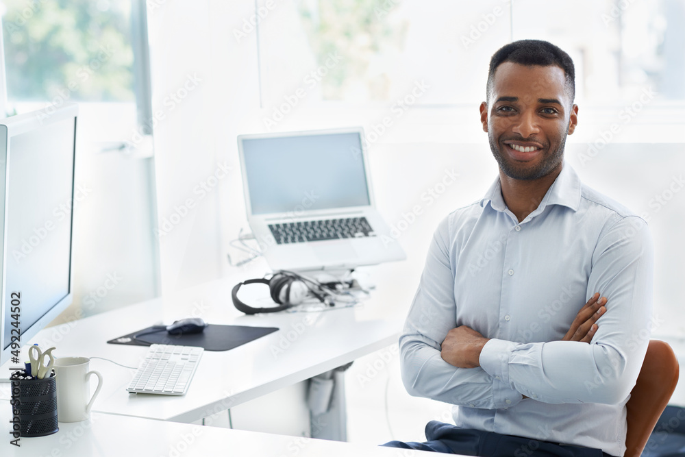 Young, modern and trendy - Todays businessman. A handsome young african american businessman sitting at his desk with his arms folded.