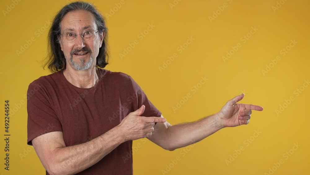 Promoter elderly gray-haired bearded man 50s 60ss red shirt point fingers aside on workspace copy space mockup promo commercial area isolated on solid yellow background studio portrait Promoter elderly gray-haired bearded man 50s 60ss red shirt point fingers aside on workspace copy space mockup promo commercial area isolated on solid yellow background studio portrait