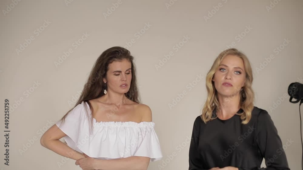 Two beautiful women are talking. One woman teaches another. Grey background, Two beautiful women are talking. One woman teaches another. Grey background,