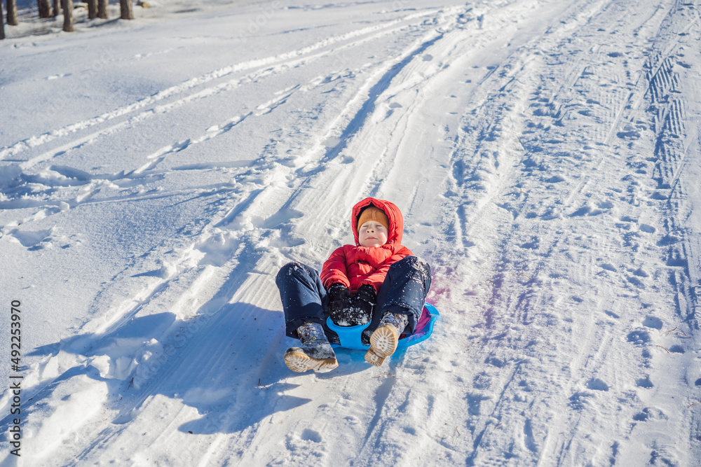 happy and positive little boy enjoying sledding and cold weather outdoor, winter fun activity concept happy and positive little boy enjoying sledding and cold weather outdoor, winter fun activity concept