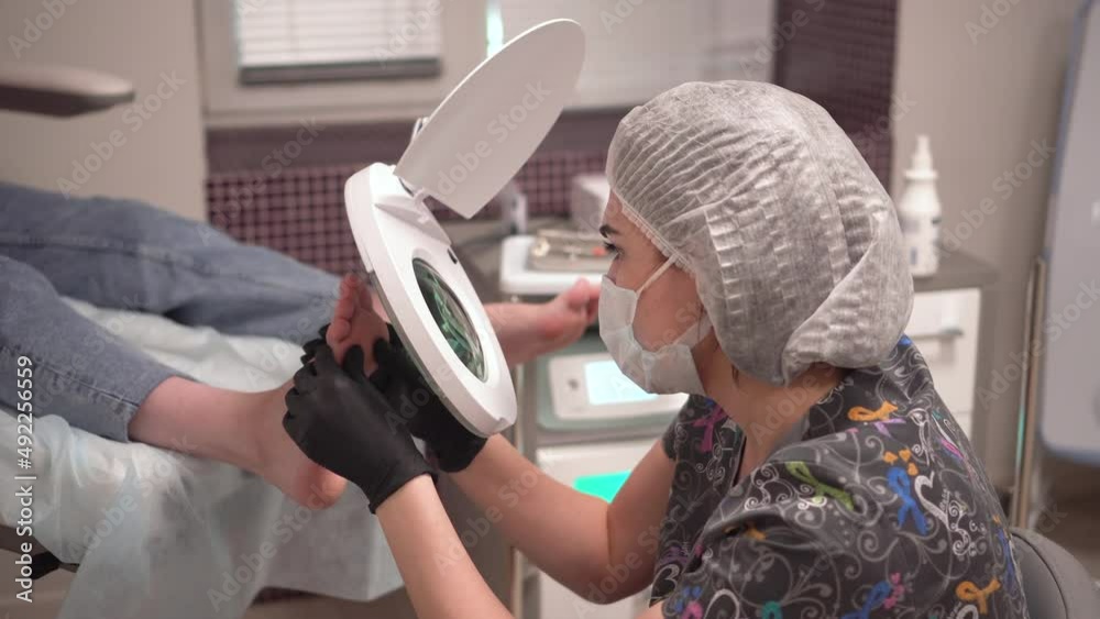 The pedicure master looks at the patient's foot through a large