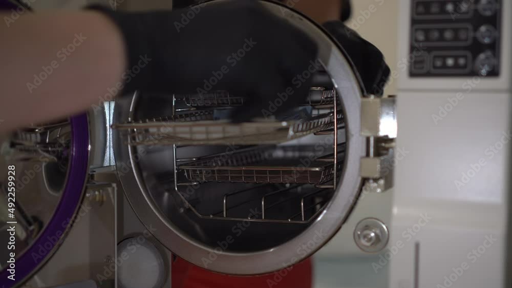 A woman puts a packaged instrument into an autoclave. Sterilization of