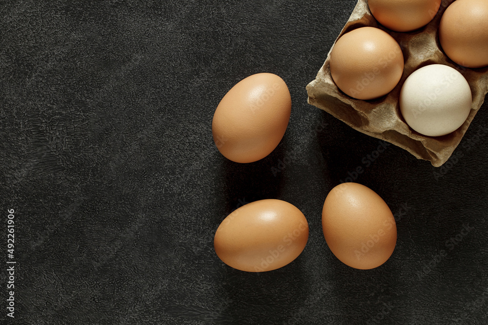 Chicken eggs whole in cardboard tray and on dark background, top view, space to copy text.. Chicken eggs whole in cardboard tray and on dark background, top view, space to copy text..