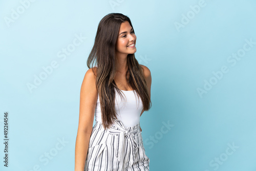 Young brazilian woman isolated on blue background looking to the side and smiling