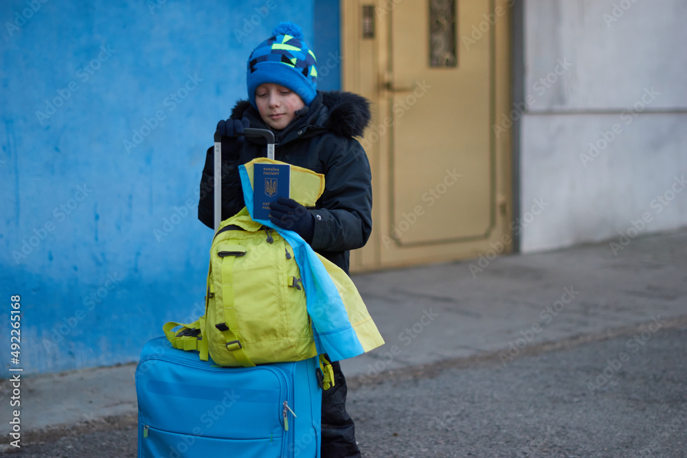 Evacuation of civilians, sad child with the flag of Ukraine. Refugee family from Ukraine crossing the border. Hand holding a passport above the luggage with yellow-blue flag. Stop war, support Ukraine