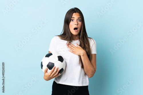 Young football player brazilian girl isolated on blue background surprised and shocked while looking right © luismolinero