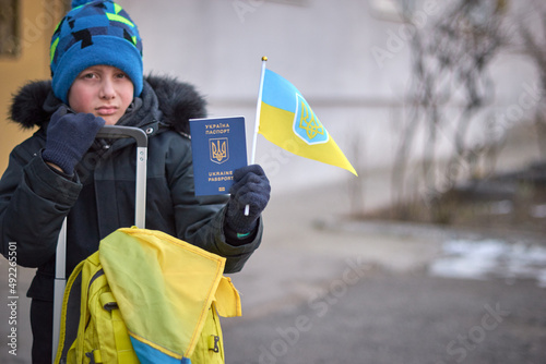 Evacuation of civilians, sad child with the flag of Ukraine. Refugee family from Ukraine crossing the border. Hand holding a passport above the luggage with yellow-blue flag. Stop war, support Ukraine