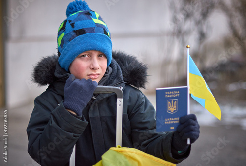 Evacuation of civilians, sad child with the flag of Ukraine. Refugee family from Ukraine crossing the border. Hand holding a passport above the luggage with yellow-blue flag. Stop war, support Ukraine