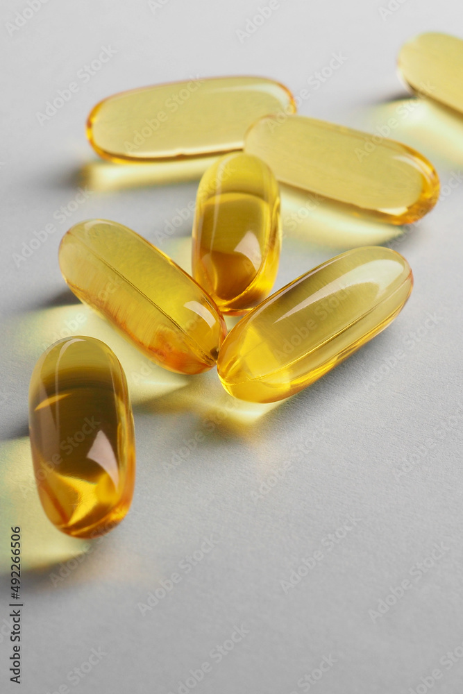 Fish oil. Yellow softgels or capsules lie on white or light gray surface. Vertical illustration about vitamins and healthy lifestyle. Softgel close-up. Omega-3 fatty acids. Macro Fish oil. Yellow softgels or capsules lie on white or light gray surface. Vertical illustration about vitamins and healthy lifestyle. Softgel close-up. Omega-3 fatty acids. Macro