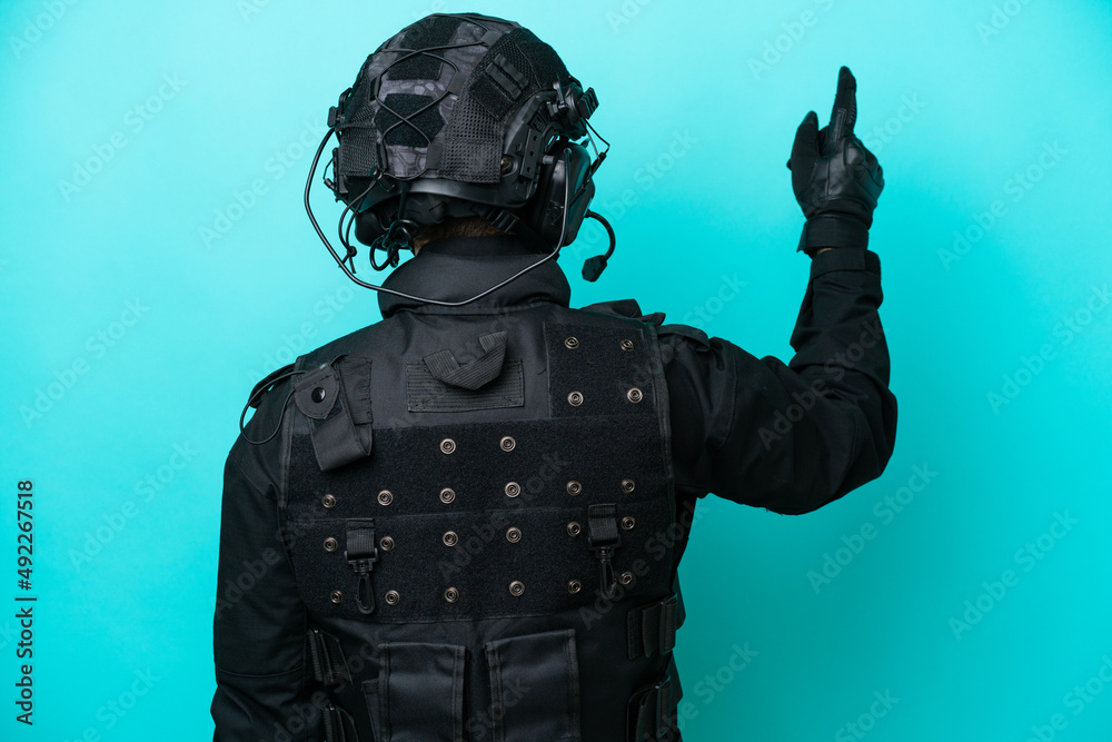SWAT caucasian man isolated on blue background pointing back with the index finger SWAT caucasian man isolated on blue background pointing back with the index finger