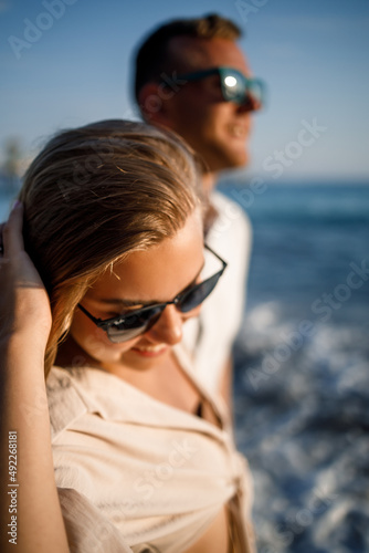 Young tanned woman in sunglasses walking along the sea coast with a man, selective focus