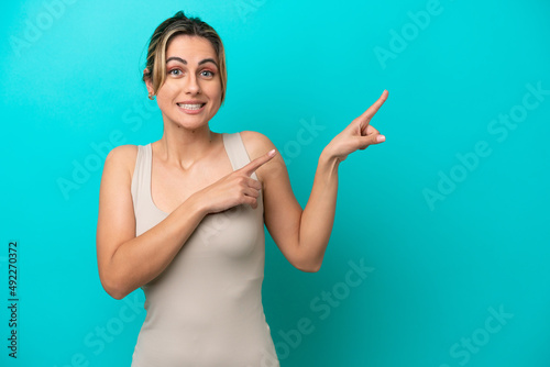 Young caucasian woman isolated on blue background frightened and pointing to the side