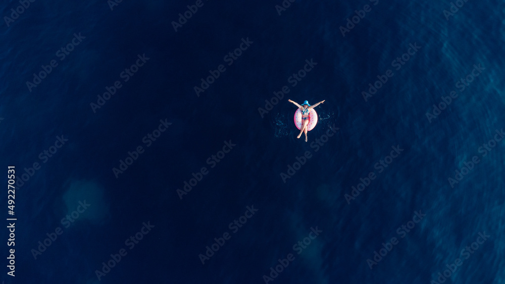 Aerial view of young brunette woman swimming on the inflatable big donut in the blue sea. Top view of slim lady relaxing on her holidays Adriatic sea.