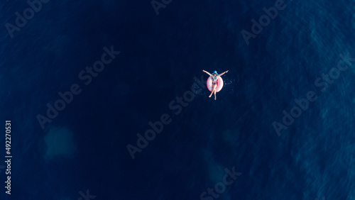 Aerial view of young brunette woman swimming on the inflatable big donut in the blue sea. Top view of slim lady relaxing on her holidays Adriatic sea.