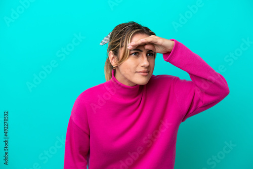 Young caucasian woman isolated on blue background looking far away with hand to look something © luismolinero