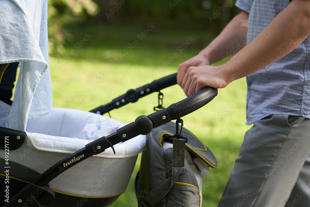 Obraz premium A young dad walking in the park with a baby in a stroller. Close-up of men's hands with a stroller. Father's Day concept. High quality photo