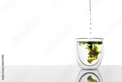 Glass of water with chlorophyll extract against white grey background. Pouring liquid chlorophyll in a glass of water. Concept of superfood, healthy eating, detox and diet. Copy space photo