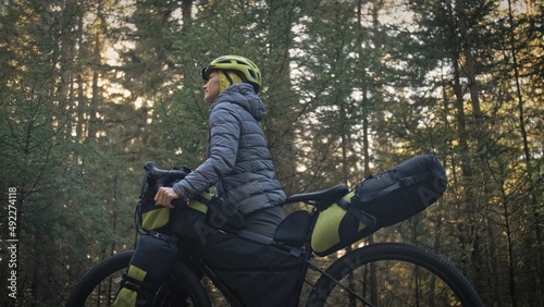 The woman travel on mixed terrain cycle touring with bike bikepacking outdoor. The traveler journey with bicycle bags. Stylish bikepacking, bike, sportswear in green black colors. Magic forest park. photo