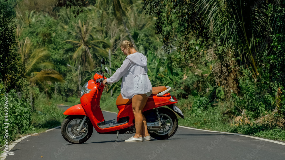 Woman on red scooter in white clothes drive on forest road trail. Dancing trip. One girl caucasian tourist in sunglasses dance, relax, rest near motorbike. Asia Thailand ride tourism. Motorcycle rent. Woman on red scooter in white clothes drive on forest road trail. Dancing trip. One girl caucasian tourist in sunglasses dance, relax, rest near motorbike. Asia Thailand ride tourism. Motorcycle rent.