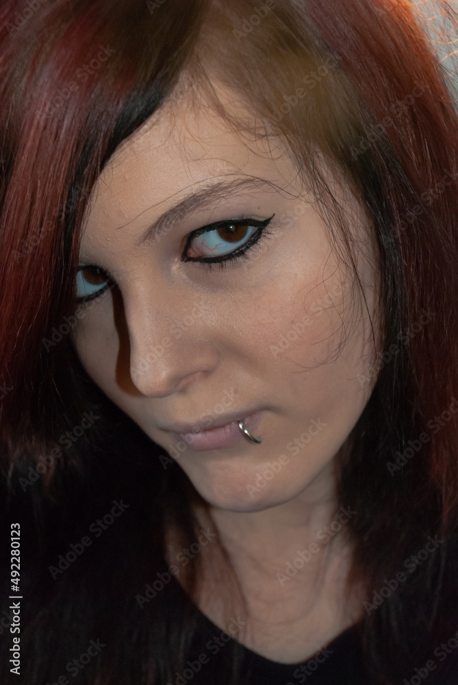 Young punk emo Girl with piercing, with red and black hair, looking at camera with serious facial expression, close-up Young punk emo Girl with piercing, with red and black hair, looking at camera with serious facial expression, close-up
