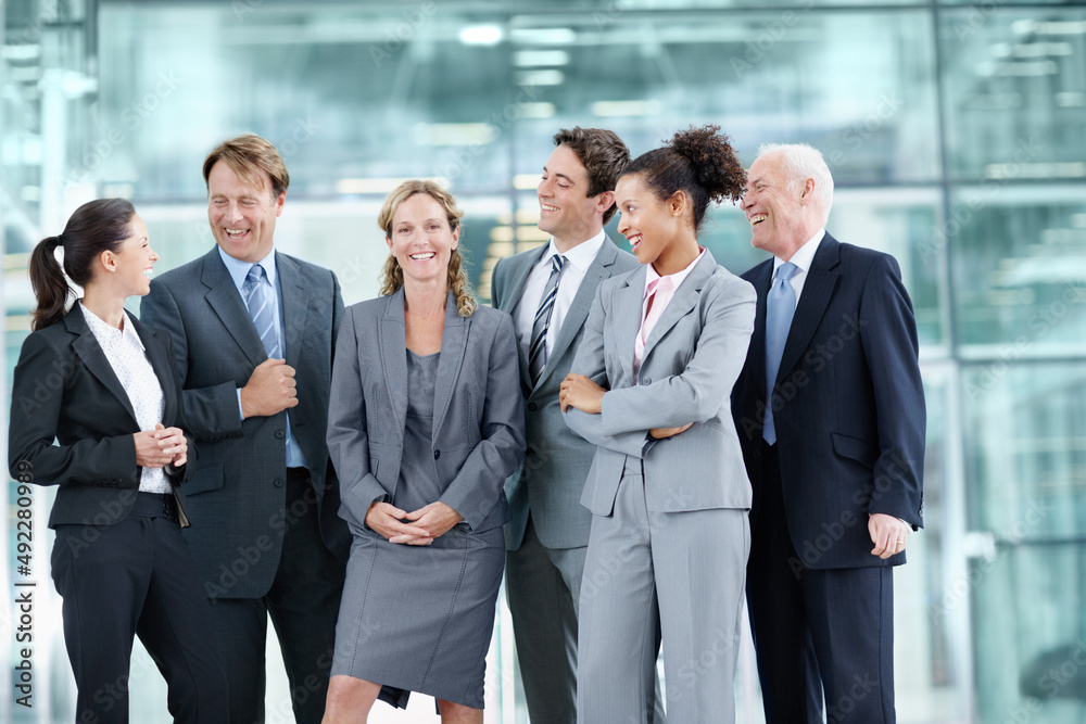 Supported by her proud team of coworkers. Positive group of businesspeople standing together and smiling while surrounding a coworker - portrait. Supported by her proud team of coworkers. Positive group of businesspeople standing together and smiling while surrounding a coworker - portrait.