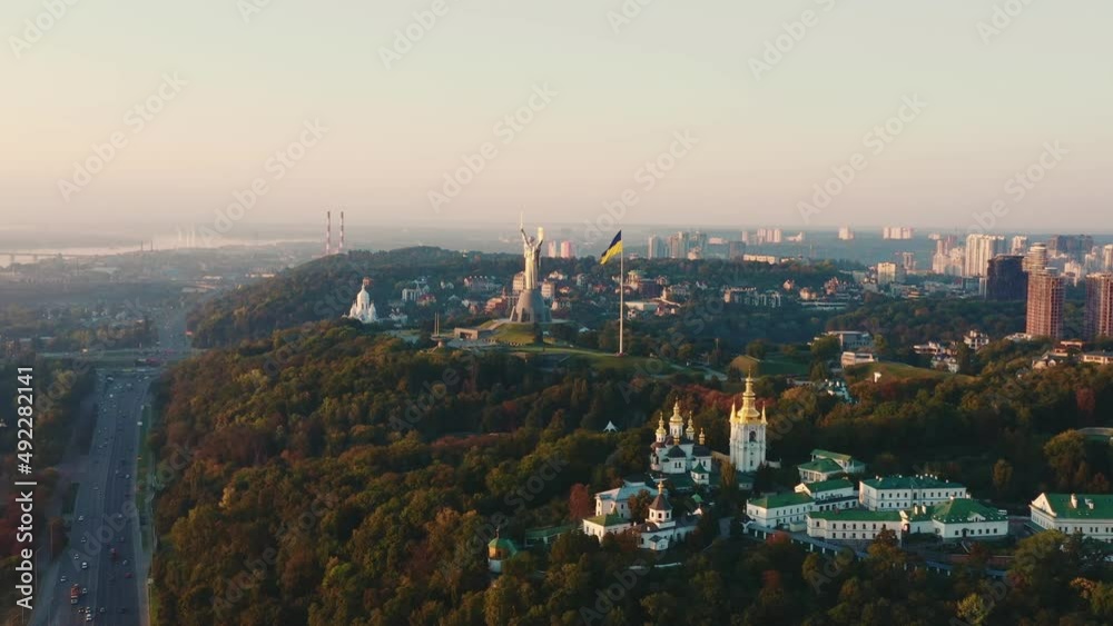 Epic sunrise aerial view of famous Motherland statue and Ukraine flag in Kyiv over beautiful peaceful summer cityscape.