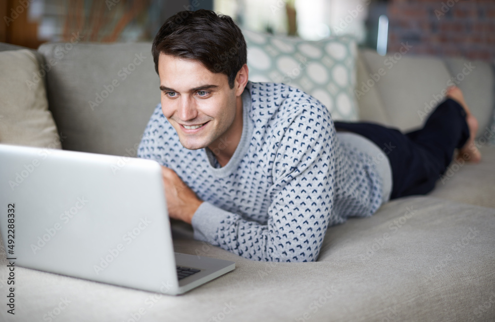 Getting excited about downloading his favorite tv series. Cropped shot of a young man using his laptop on his sofa. Getting excited about downloading his favorite tv series. Cropped shot of a young man using his laptop on his sofa.