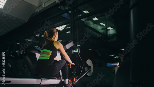 Fit Athletic Baby Woman Work out on Rowing Machine, Doing Her Fitness Exercise. Girl Activity Training in Modern Gym. Sports Female Workout in Exercising on Row Machine Fitness Center.