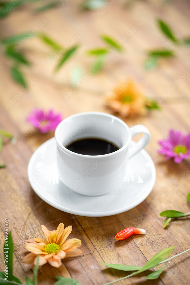 A white cup is set on a wooden table decorated with flowers. A white cup is set on a wooden table decorated with flowers.