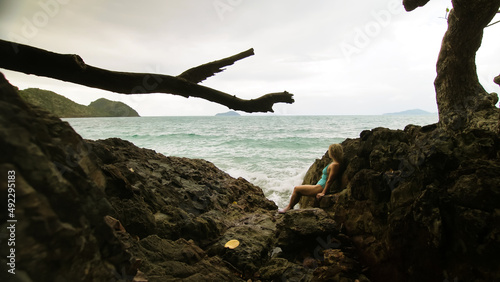 Pretty woman meditates, relaxes on rock crack reef hill in stormy morning cloudy sea. Concept feminine, sexual vaginal health, hygiene, womanly, freedom, fresh. Mother of ocean gives birth to him
