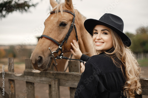 Woman touching a brown horse behinde the fence on a farm © hetmanstock2