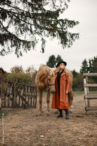 Woman in red leather coat touching a brown horse on a farm