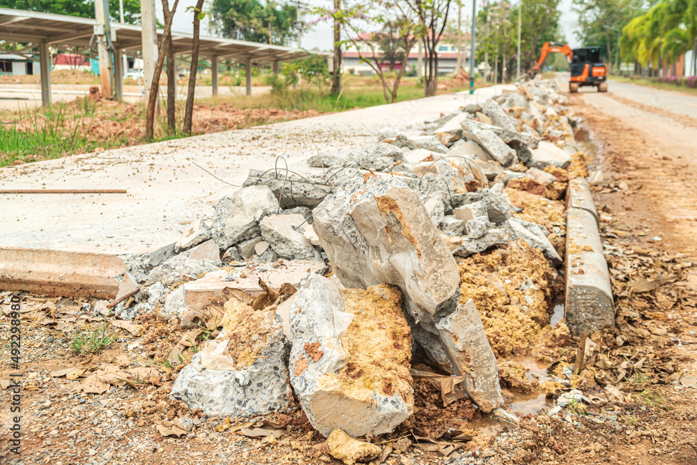 Fototapeta premium Focus on broken concrete fragments and blur the punching car running in front. Drilling and demolishing the concrete pavement of the roadside pavement.