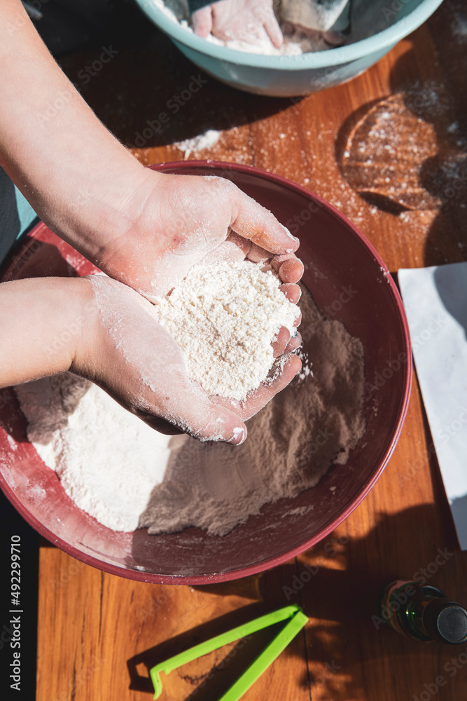 Fototapeta premium Child's hands holding flour above a bowl of play dough mix