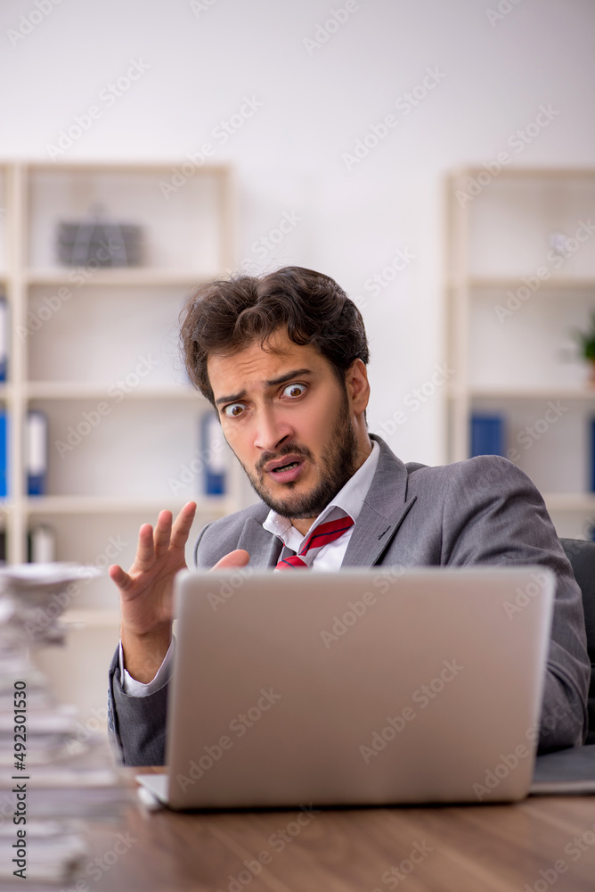 Young male employee unhappy with excessive work in the office Young male employee unhappy with excessive work in the office