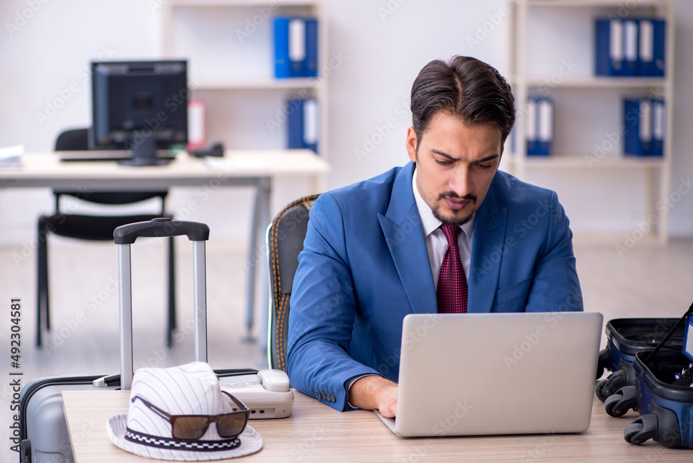 Young male employee preparing for trip at workplace Young male employee preparing for trip at workplace