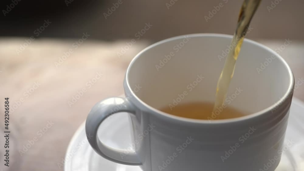 Pour tea from a clear glass teapot into a ceramic teacup. Healthy drink concept. Pour tea from a clear glass teapot into a ceramic teacup. Healthy drink concept.