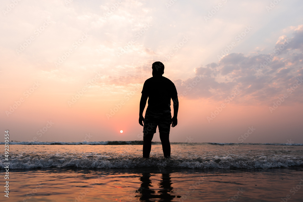 silhouette of man walking on the beach at sunset