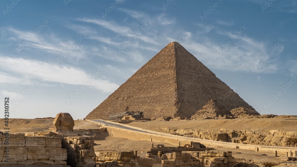 The pyramid of Mycerinus on the background of the blue sky. Nearby are the pyramids of queens. The highway passes through the desert. In the foreground are the ruins of the temple of the Sphinx. Egypt