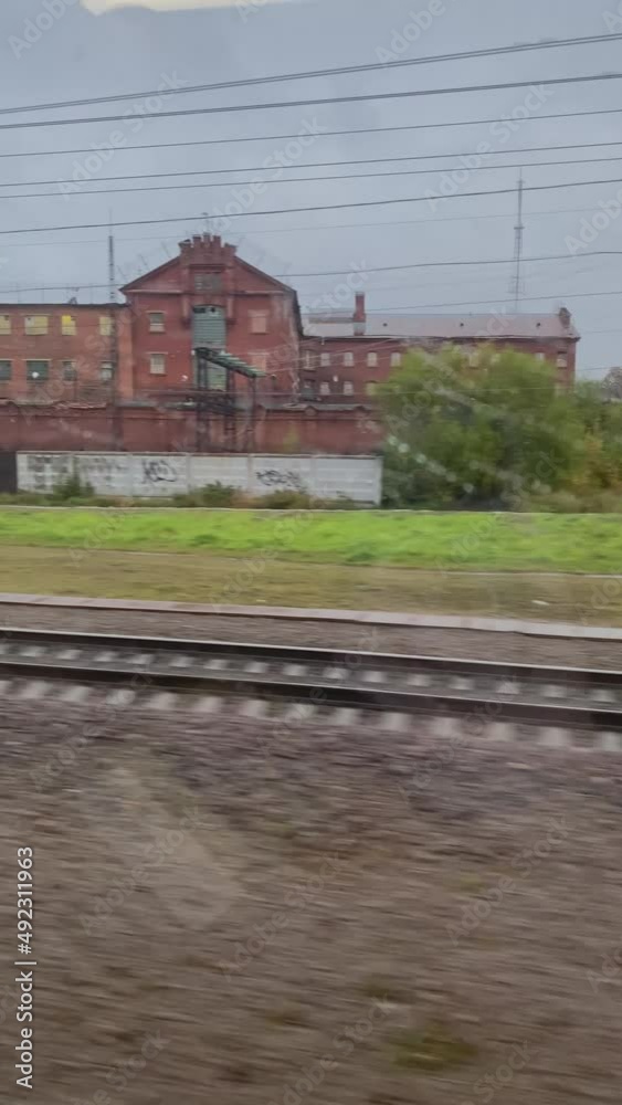 View from window of movement train to countryside and railways. Travel by locomotive past picturesque landscape. Village, factory building, autumn trees and gray cloudy sky. View from window of movement train to countryside and railways. Travel by locomotive past picturesque landscape. Village, factory building, autumn trees and gray cloudy sky.